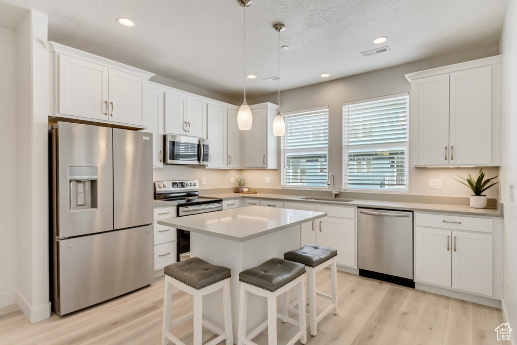 Kitchen with white cabinets, a center island, decorative light fixtures, and stainless steel appliances