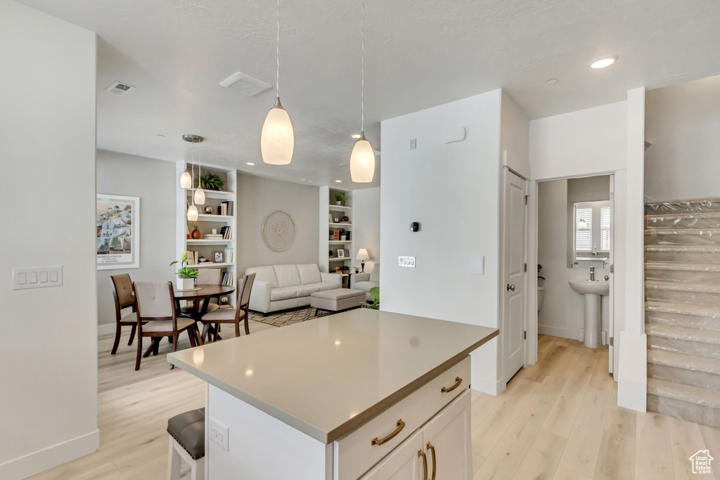 Kitchen featuring pendant lighting, light wood-type flooring, a kitchen island, built in shelves, and white cabinets
