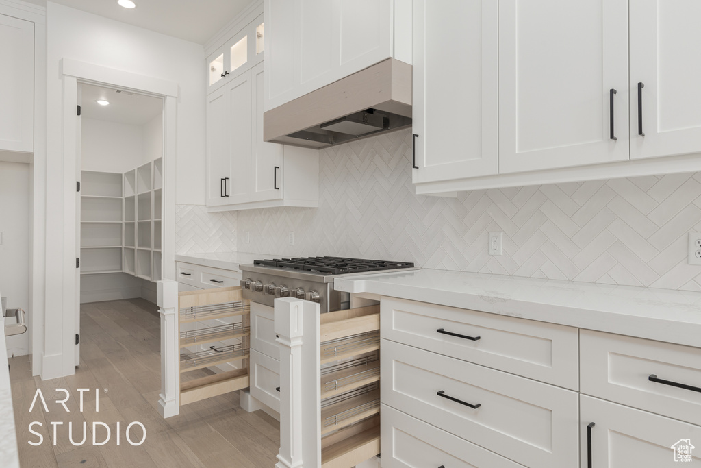 Kitchen with light stone countertops, premium range hood, backsplash, white cabinets, and light wood-type flooring