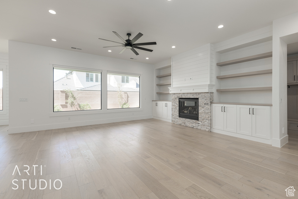 Unfurnished living room featuring light hardwood / wood-style flooring, built in features, ceiling fan, and a large fireplace