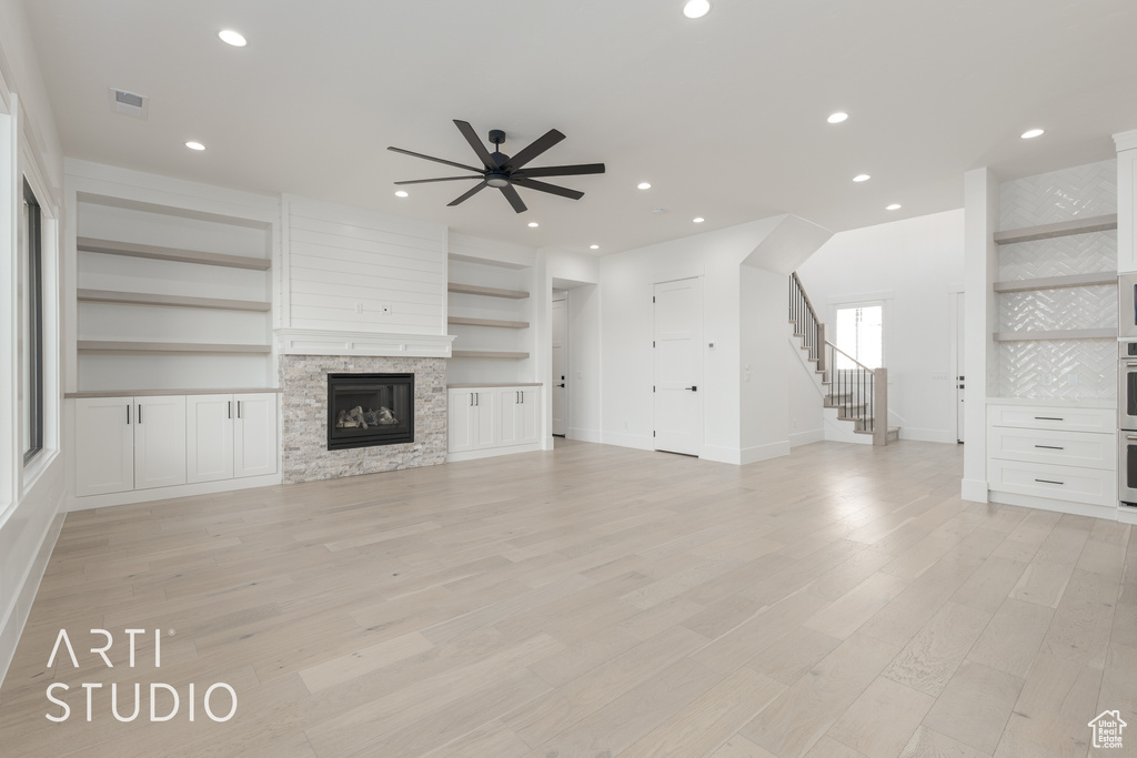 Unfurnished living room with light hardwood / wood-style floors, ceiling fan, a stone fireplace, and built in shelves