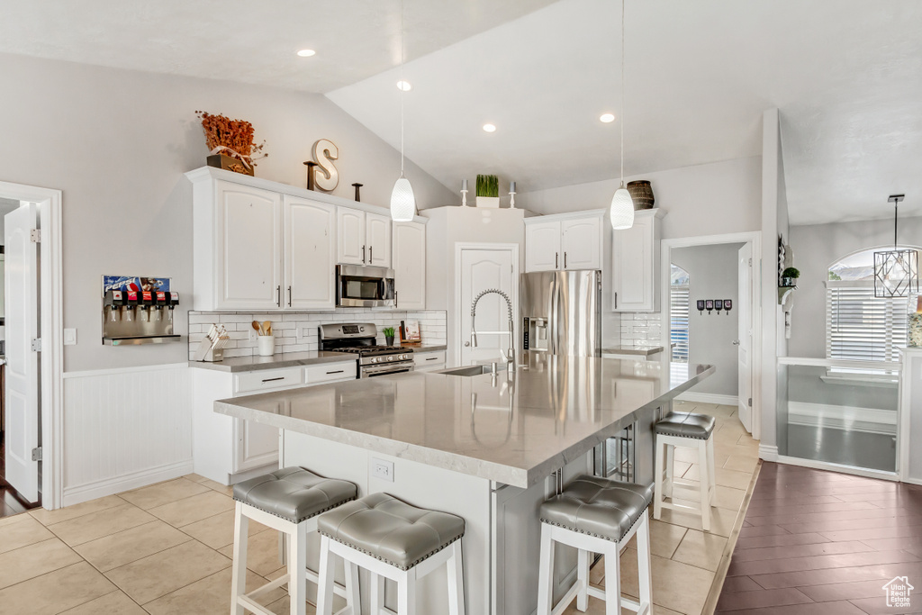 Kitchen with pendant lighting, light wood-type flooring, appliances with stainless steel finishes, white cabinets, and lofted ceiling