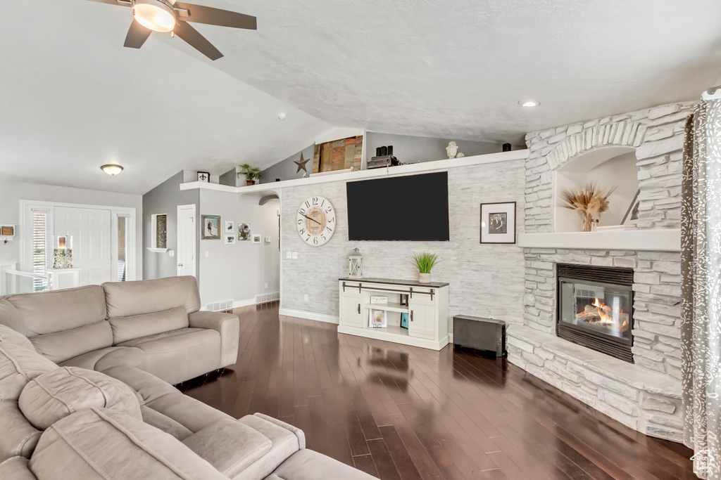 Living room featuring dark wood-type flooring, ceiling fan, vaulted ceiling, and a fireplace