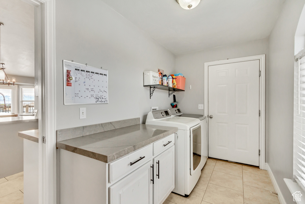 Washroom with an inviting chandelier, washing machine and dryer, cabinets, and light tile floors
