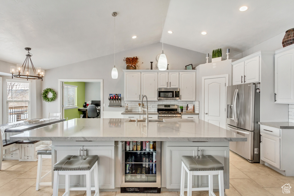 Kitchen featuring a chandelier, stainless steel appliances, a kitchen bar, a center island with sink, and white cabinetry