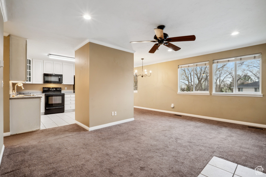 Interior space featuring ceiling fan with notable chandelier, white cabinets, range with electric stovetop, crown molding, and light colored carpet
