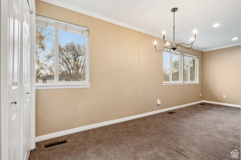 Carpeted empty room featuring a notable chandelier and crown molding