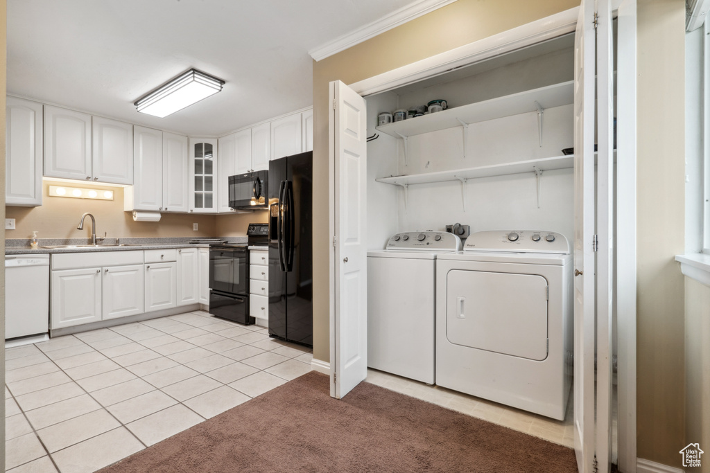 Washroom with crown molding, light tile floors, washing machine and clothes dryer, and sink