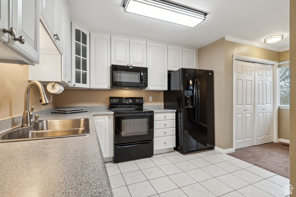 Kitchen featuring white cabinetry, black appliances, sink, light tile floors, and ornamental molding