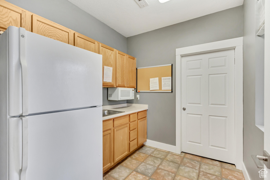 Kitchen featuring light brown cabinets, white appliances, light tile flooring, and sink