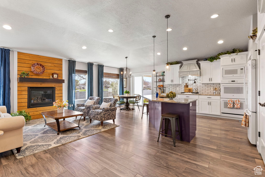 Interior space with dark hardwood / wood-style floors, white appliances, hanging light fixtures, white cabinets, and premium range hood