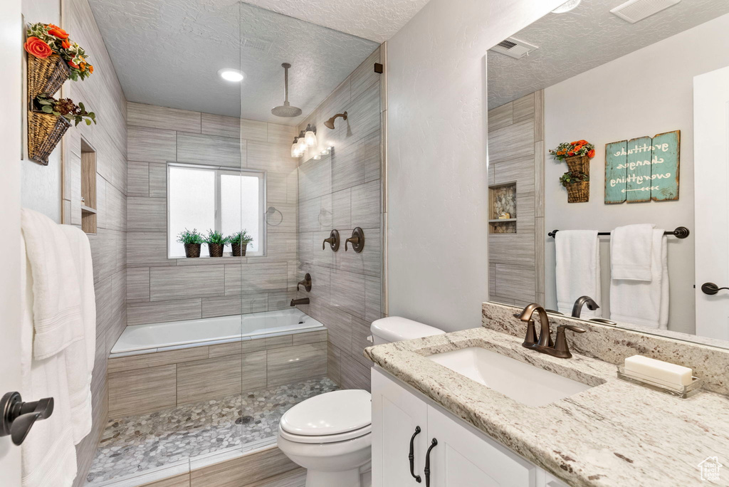 Full bathroom with a textured ceiling, toilet, enclosed tub / shower combo, and vanity
