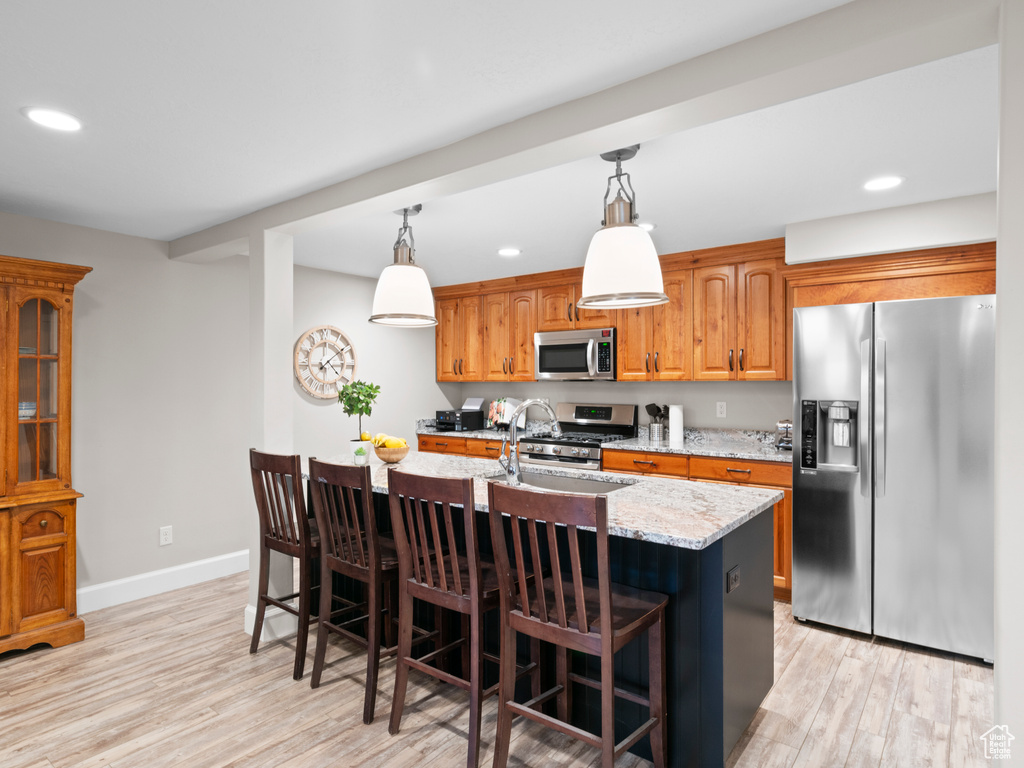 Kitchen featuring a kitchen bar, hanging light fixtures, light hardwood / wood-style flooring, and stainless steel appliances