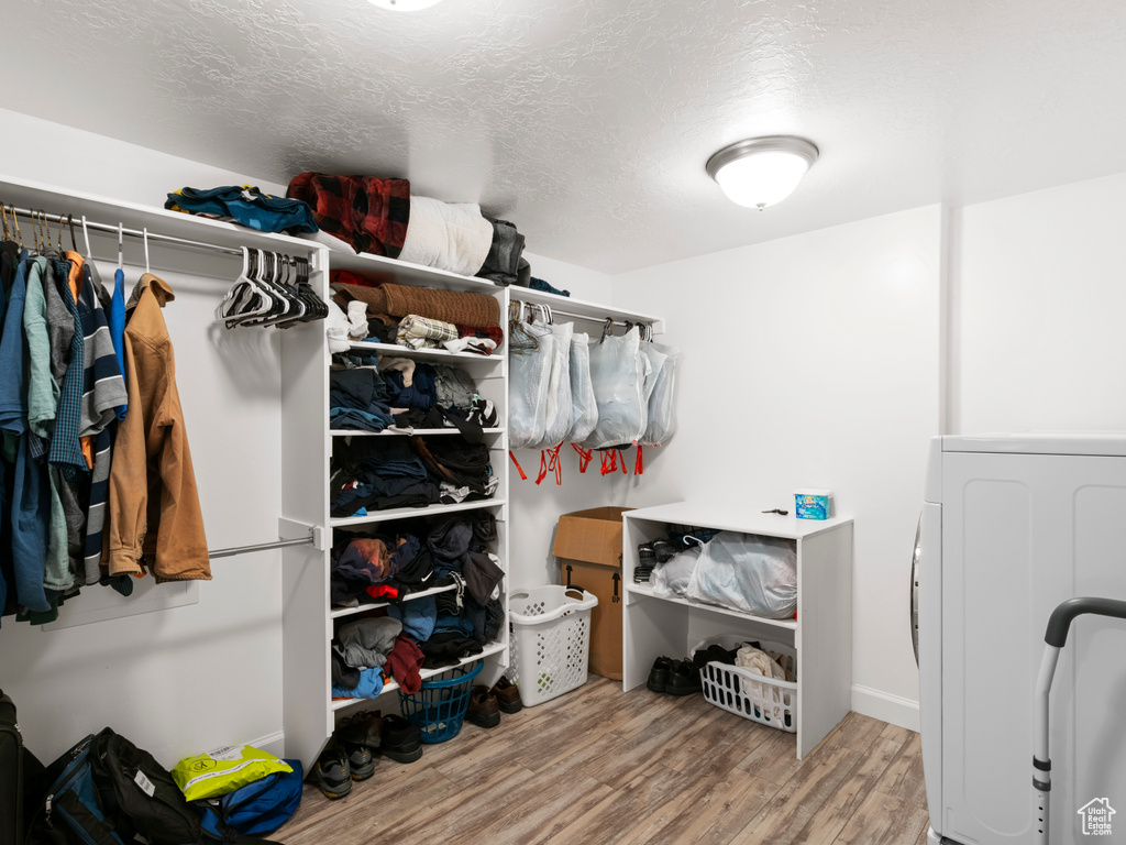 Walk in closet with washer / dryer and light hardwood / wood-style flooring