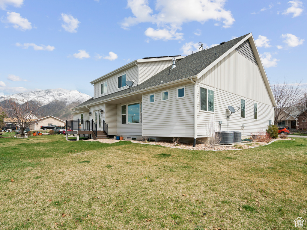 Rear view of property featuring a lawn, a deck with mountain view, and central AC unit