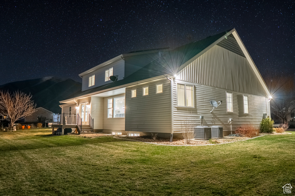 Back house at night featuring central AC and a lawn