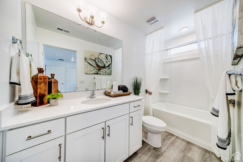 Full bathroom with toilet, vanity with extensive cabinet space, shower / bath combination with curtain, a notable chandelier, and hardwood / wood-style flooring