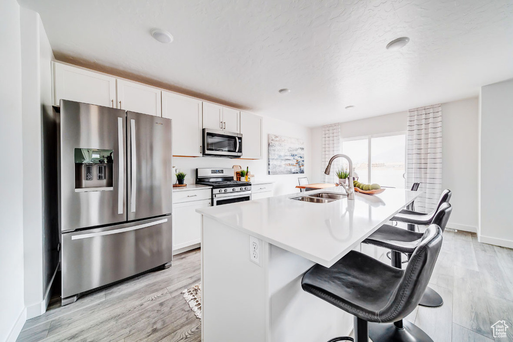 Kitchen with appliances with stainless steel finishes, white cabinets, a breakfast bar area, a center island with sink, and light wood-type flooring
