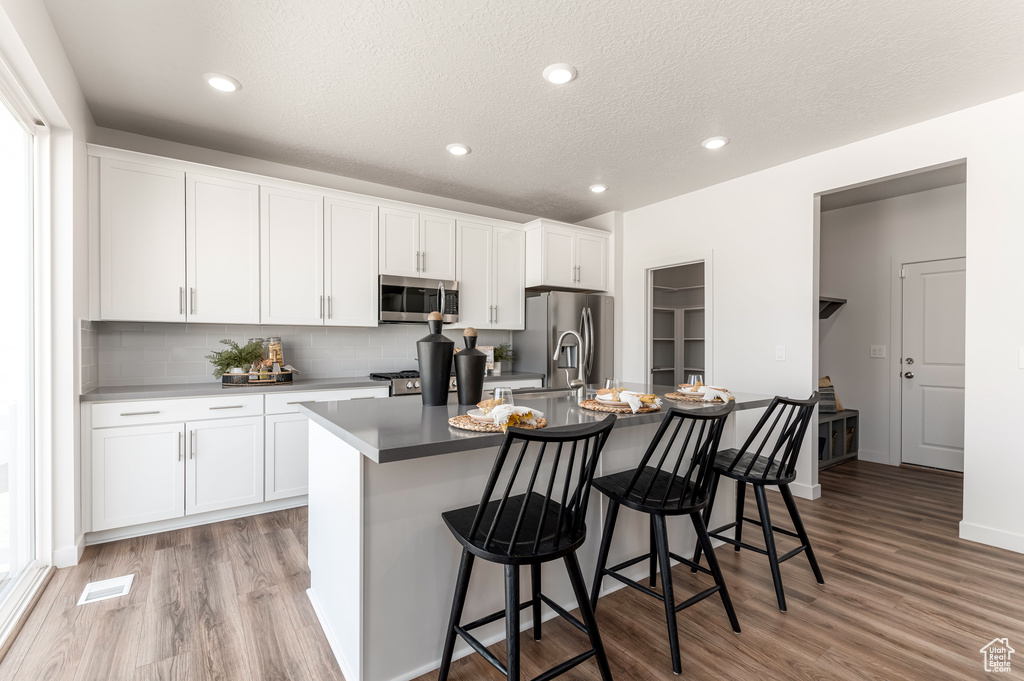 Kitchen with a breakfast bar, white cabinetry, stainless steel appliances, light hardwood / wood-style flooring, and a kitchen island with sink