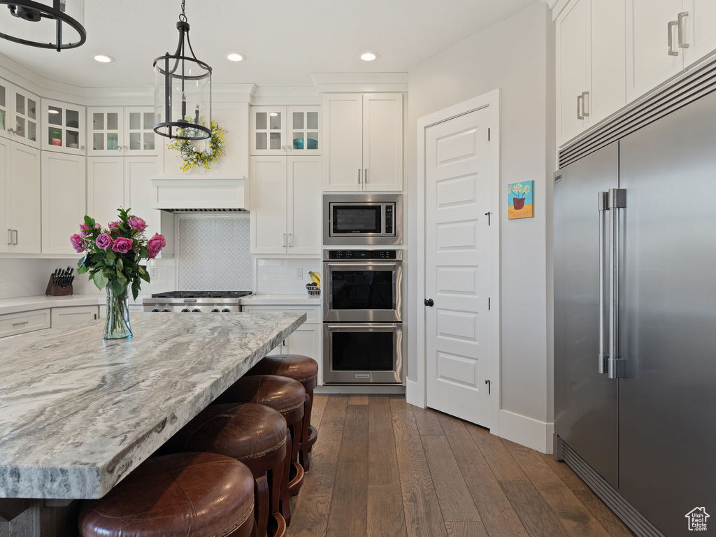 Kitchen with decorative light fixtures, dark wood-type flooring, white cabinets, tasteful backsplash, and built in appliances