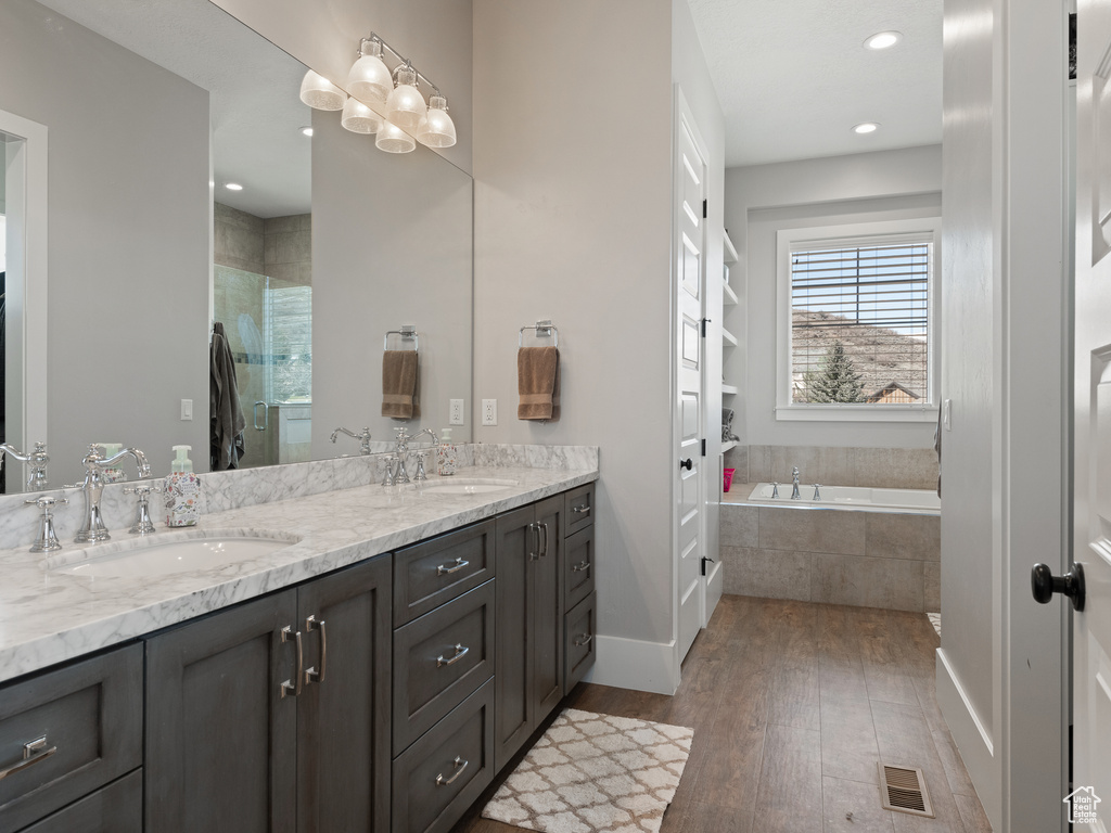 Bathroom with tiled tub, double sink, large vanity, and hardwood / wood-style flooring