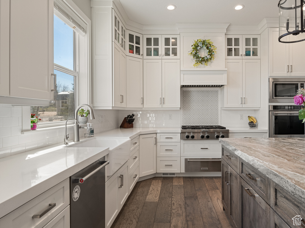 Kitchen with decorative light fixtures, appliances with stainless steel finishes, white cabinets, light stone countertops, and backsplash