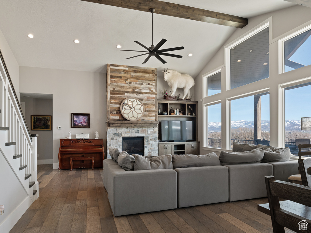 Living room with ceiling fan, beamed ceiling, dark wood-type flooring, high vaulted ceiling, and a stone fireplace