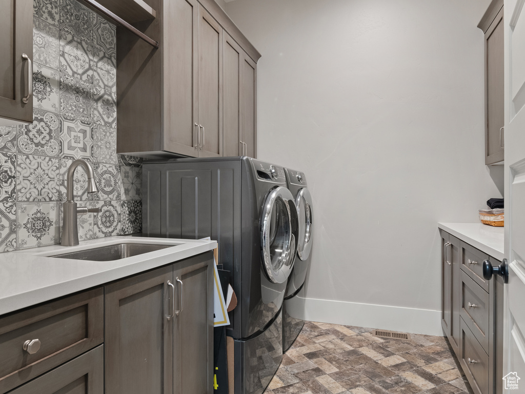 Clothes washing area featuring cabinets, sink, and washer and clothes dryer