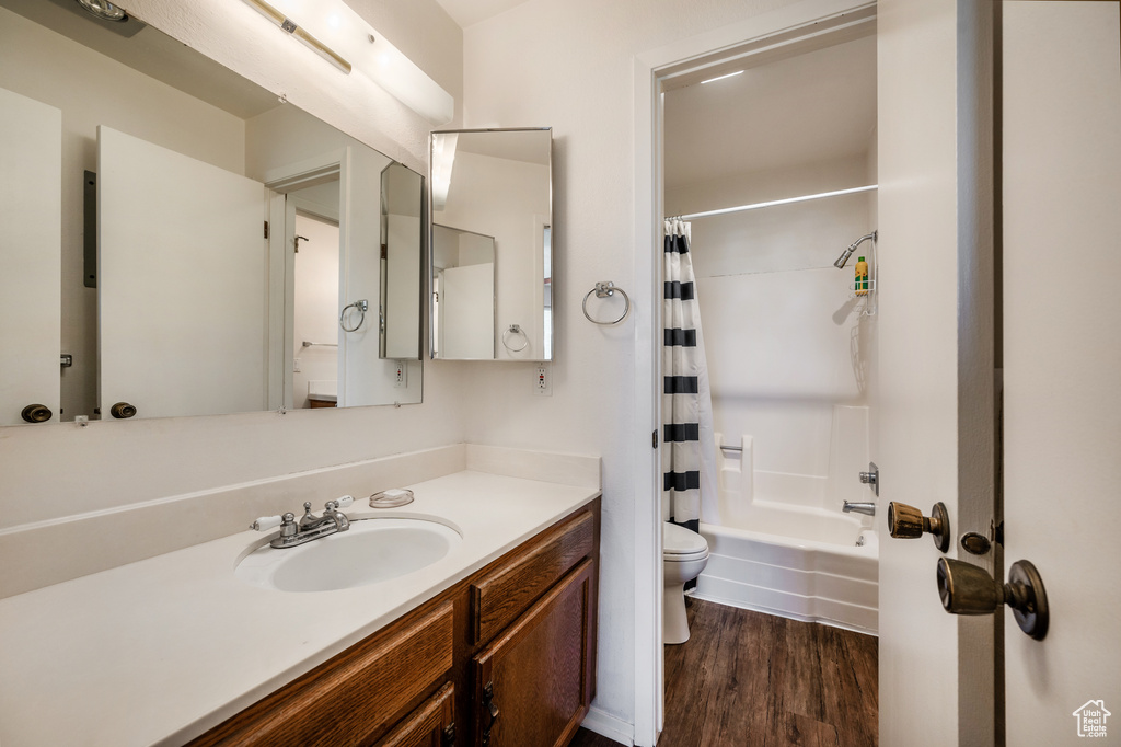 Full bathroom with toilet, shower / tub combo, large vanity, and hardwood / wood-style flooring