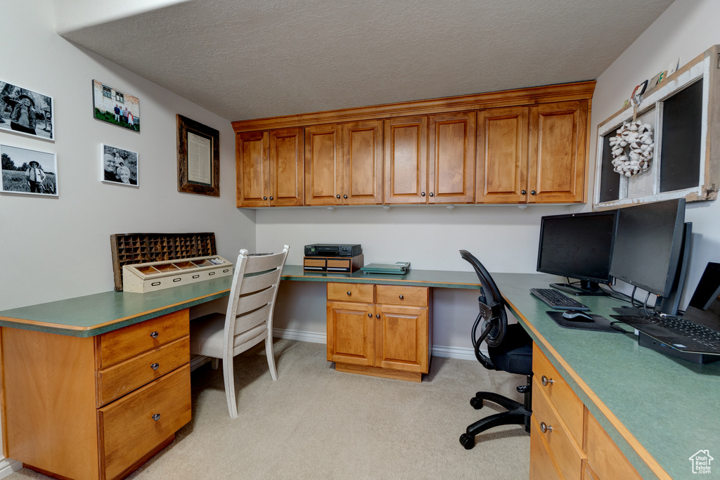 Carpeted home office with a textured ceiling and built in desk