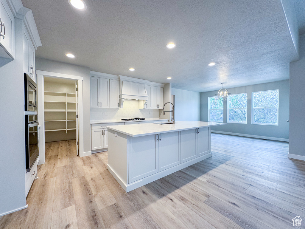 Kitchen featuring light hardwood / wood-style floors, stainless steel appliances, a center island with sink, white cabinets, and sink