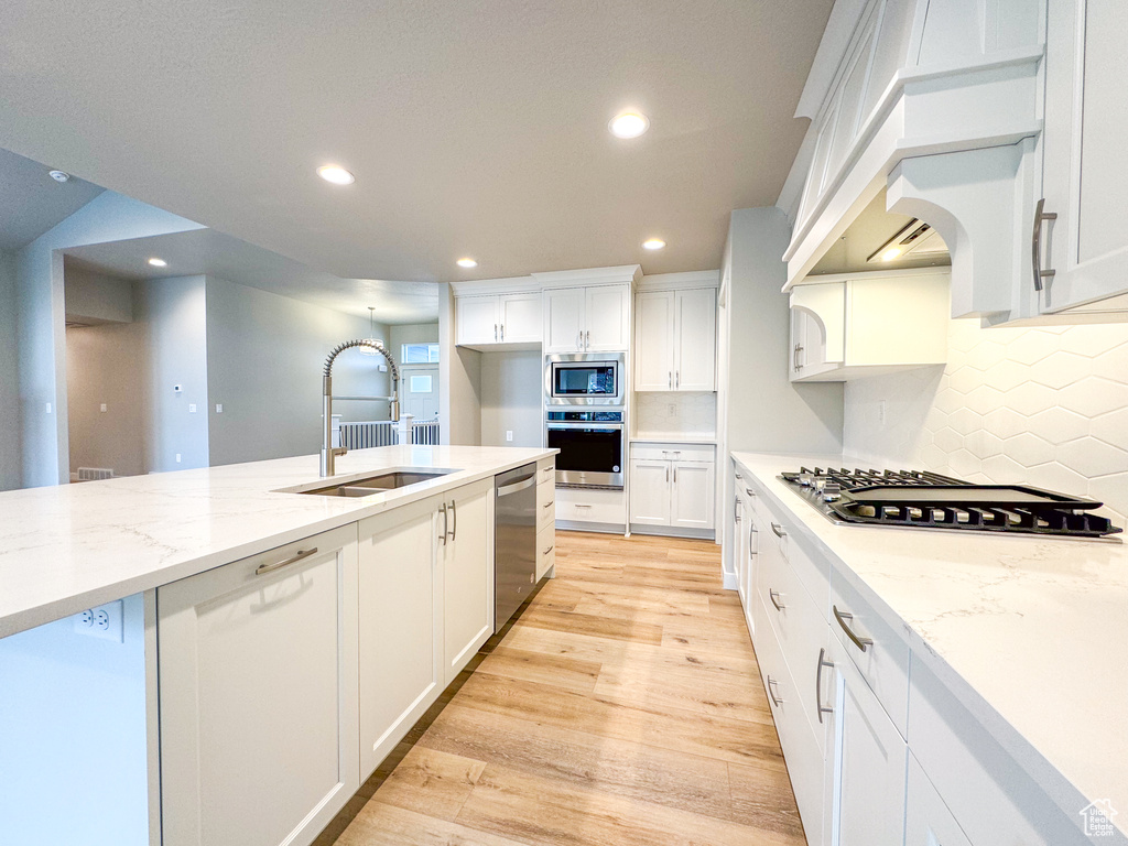 Kitchen featuring light hardwood / wood-style floors, light stone countertops, appliances with stainless steel finishes, white cabinets, and sink