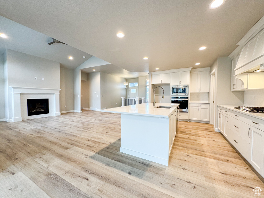 Kitchen with a center island with sink, white cabinetry, stainless steel appliances, and light wood-type flooring