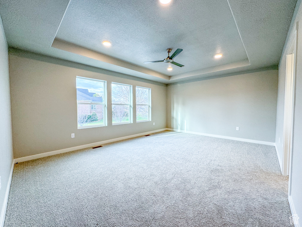 Carpeted spare room with a tray ceiling, ceiling fan, and a textured ceiling