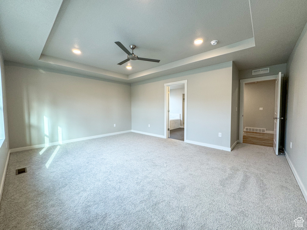 Unfurnished bedroom with light carpet, a raised ceiling, ceiling fan, and connected bathroom