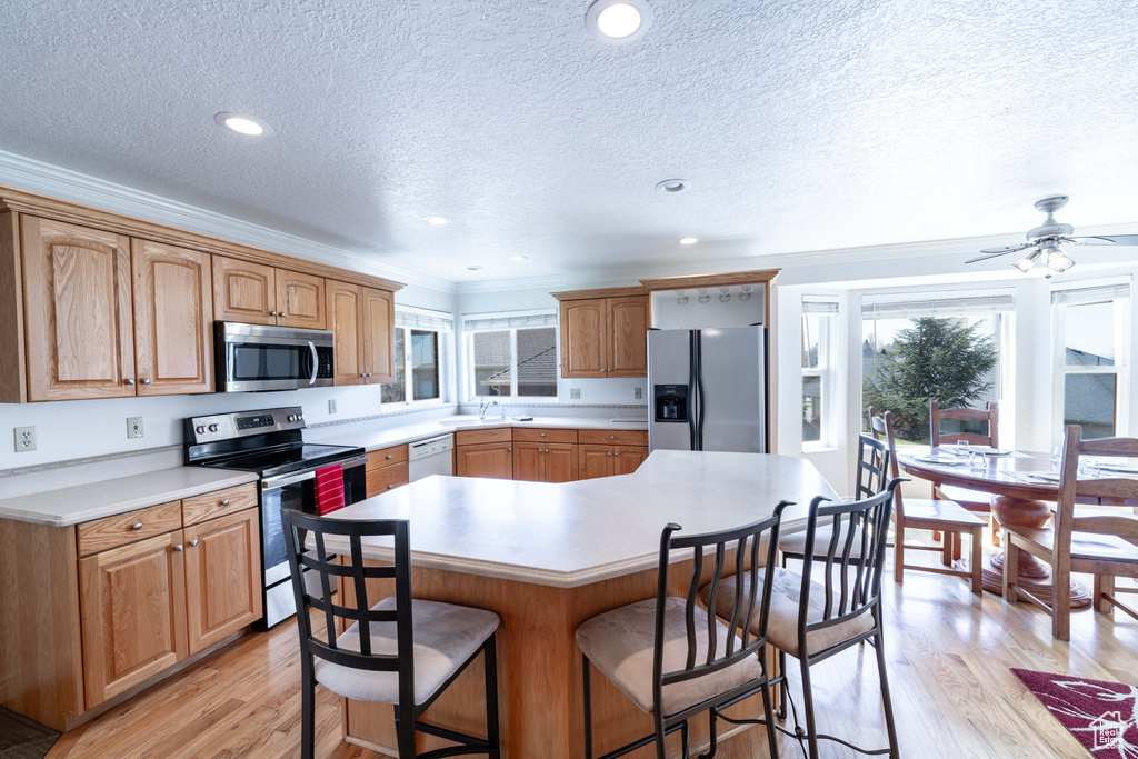 Kitchen featuring ceiling fan, a breakfast bar, appliances with stainless steel finishes, light hardwood / wood-style flooring, and a center island