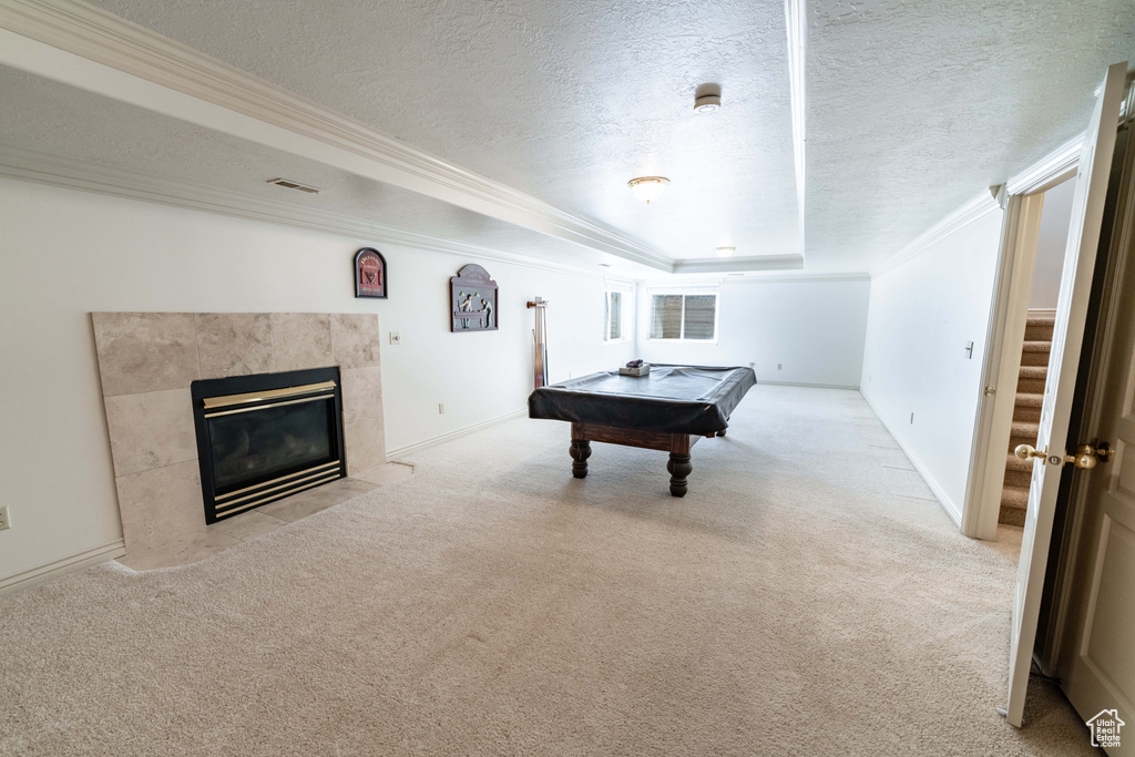 Playroom with a tile fireplace, billiards, crown molding, light carpet, and a raised ceiling