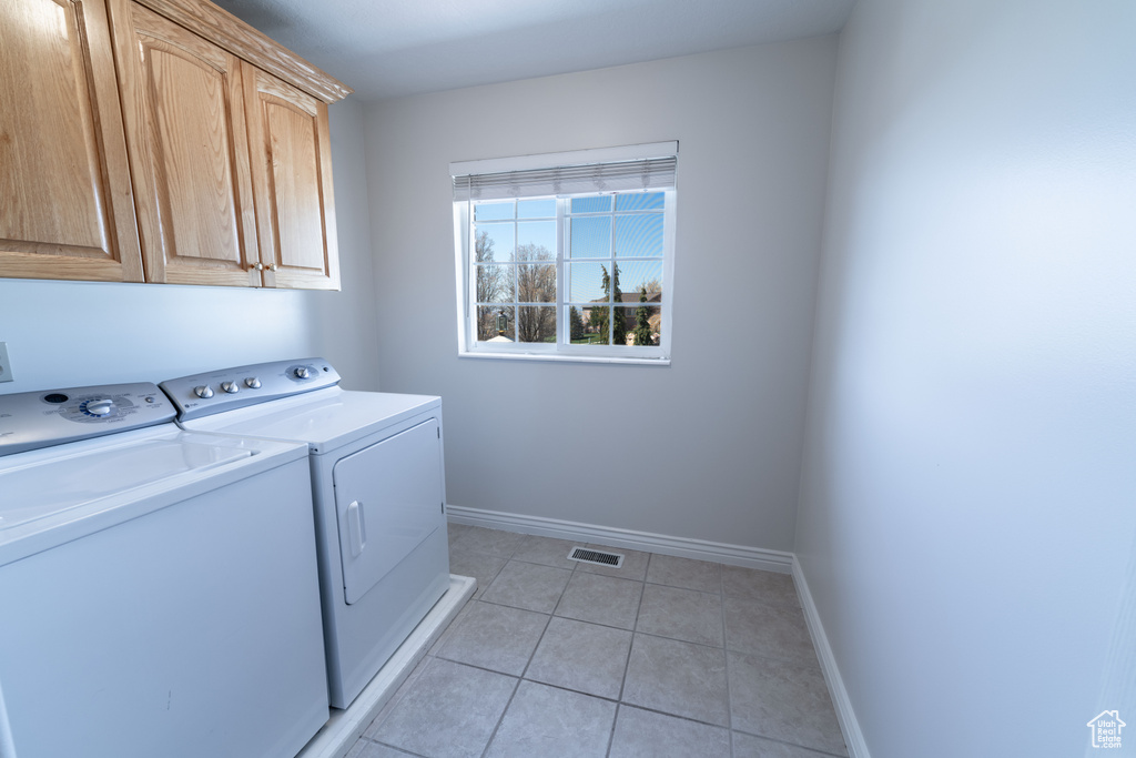 Clothes washing area featuring light tile floors, washing machine and dryer, and cabinets