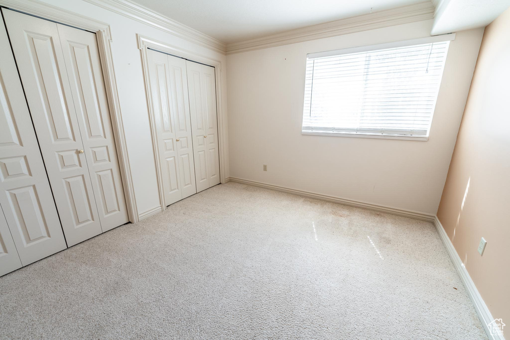 Unfurnished bedroom featuring two closets, ornamental molding, and light carpet