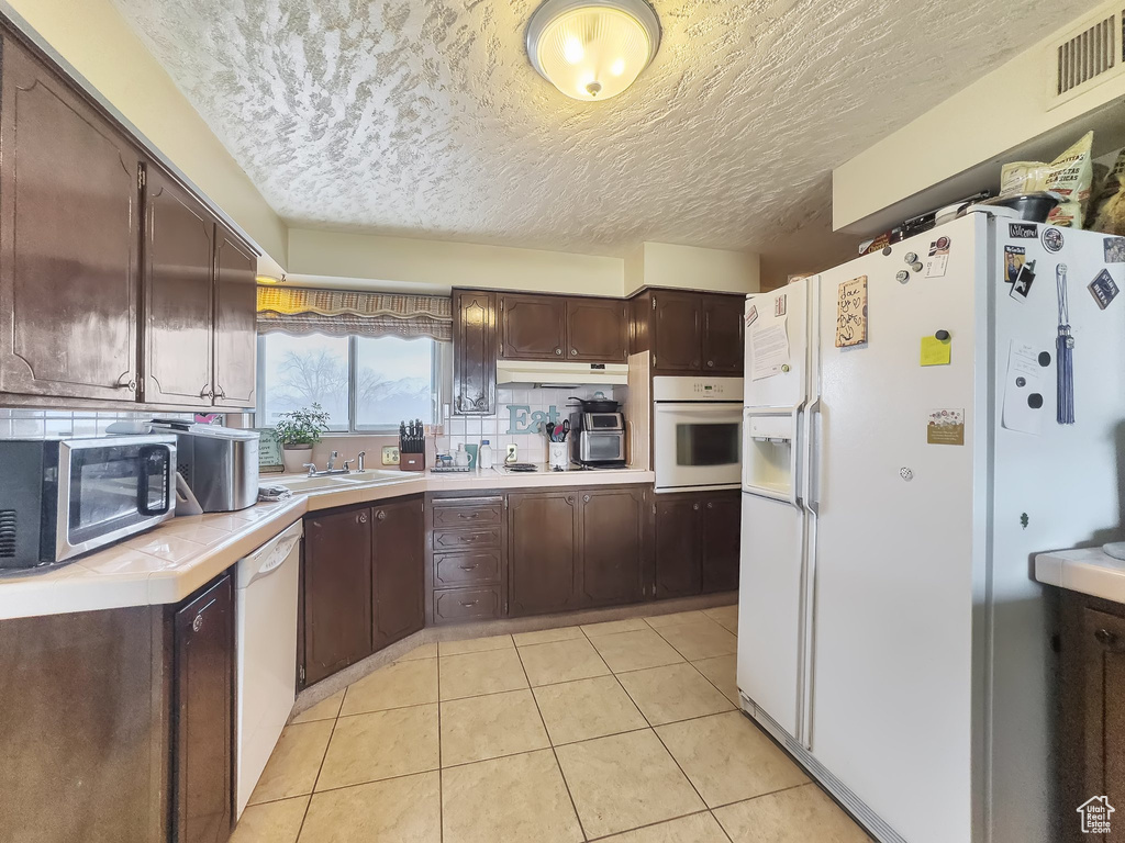 Kitchen with white appliances, light tile floors, tasteful backsplash, and dark brown cabinets
