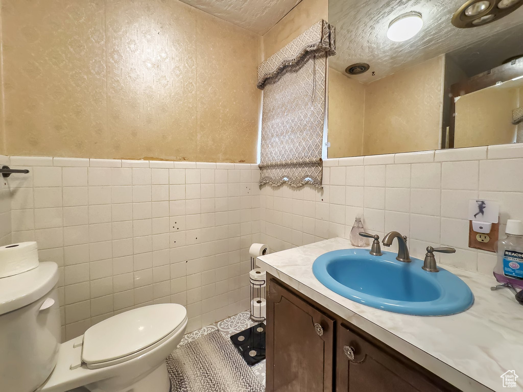 Bathroom with tile walls, toilet, backsplash, and vanity