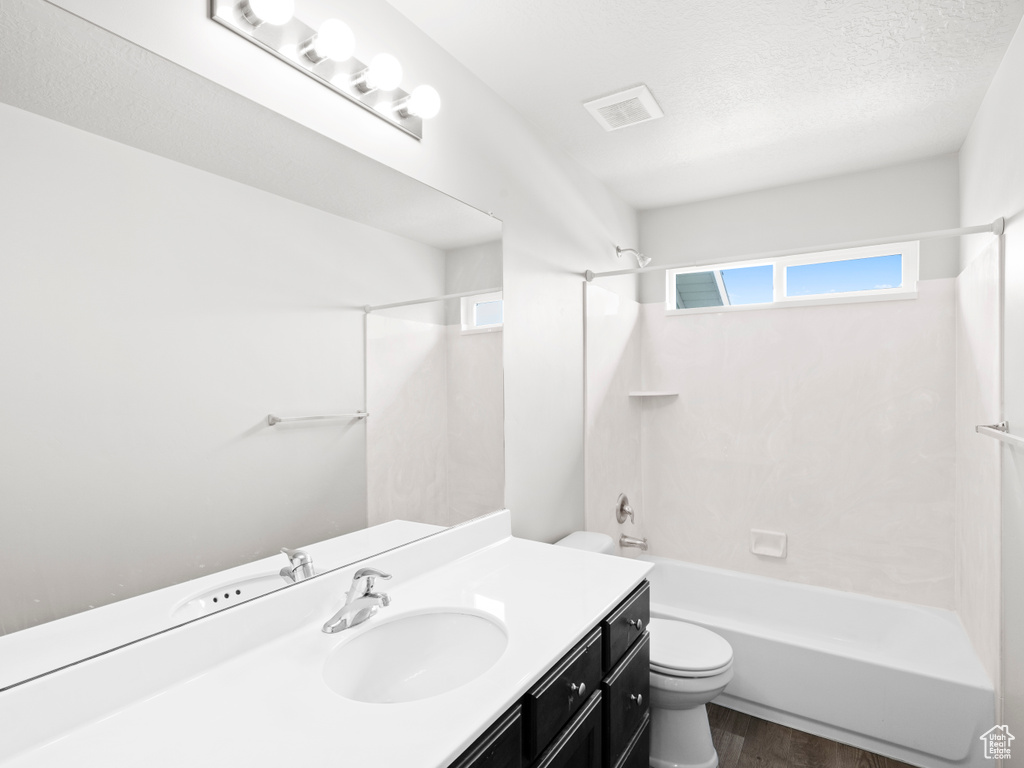 Full bathroom with shower / tub combination, wood-type flooring, a textured ceiling, vanity with extensive cabinet space, and toilet