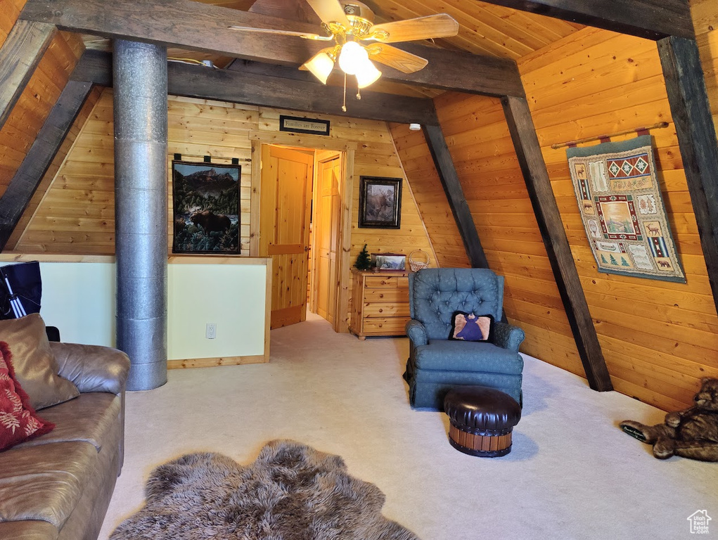 Carpeted living room with wooden walls, vaulted ceiling with beams, and ceiling fan