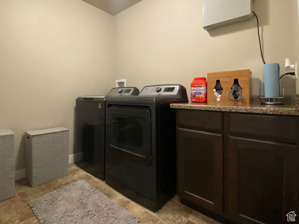 Clothes washing area featuring washer and clothes dryer, cabinets, and light tile floors