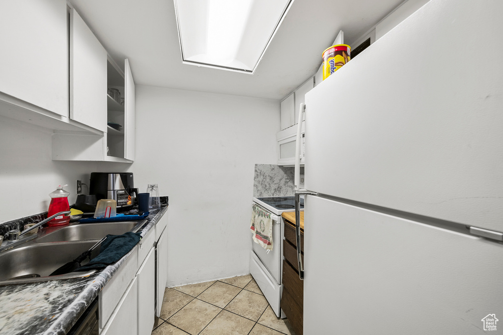 Kitchen with white appliances, white cabinets, sink, and light tile flooring