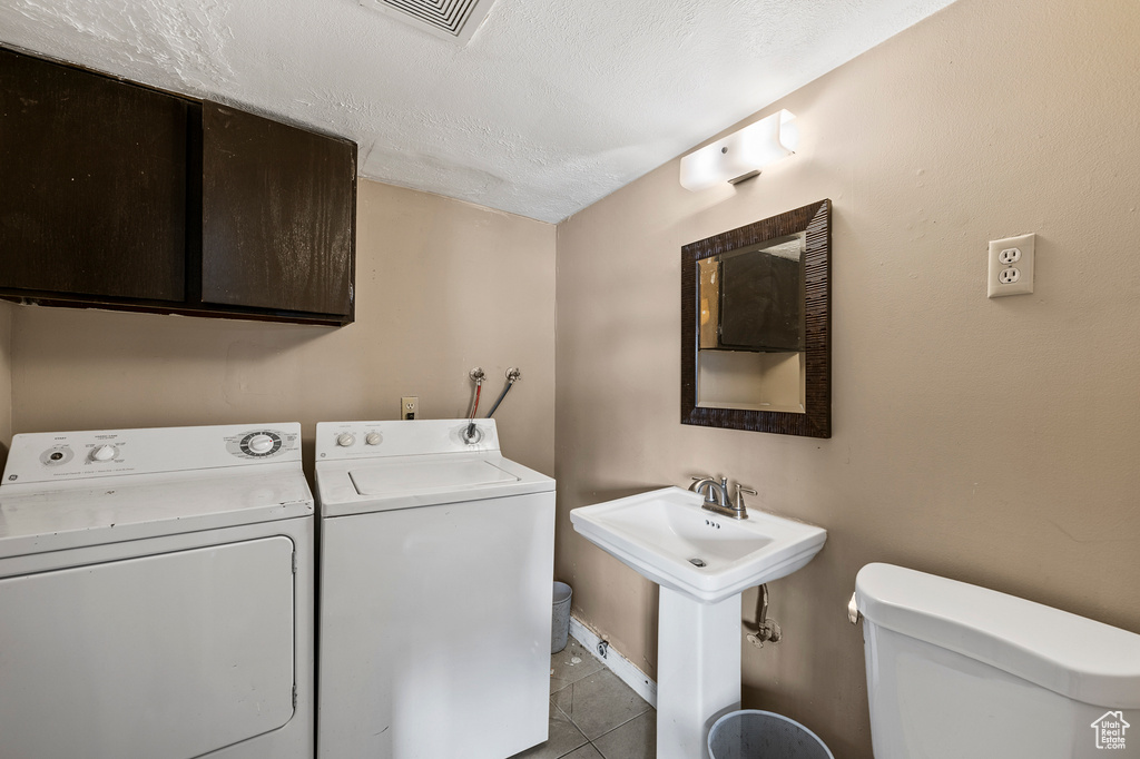 Laundry area with light tile floors, washing machine and dryer, a textured ceiling, and sink