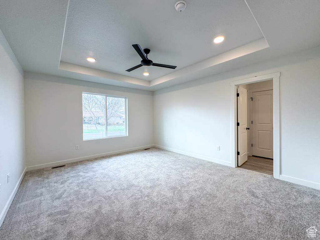 Empty room with ceiling fan, light carpet, and a raised ceiling