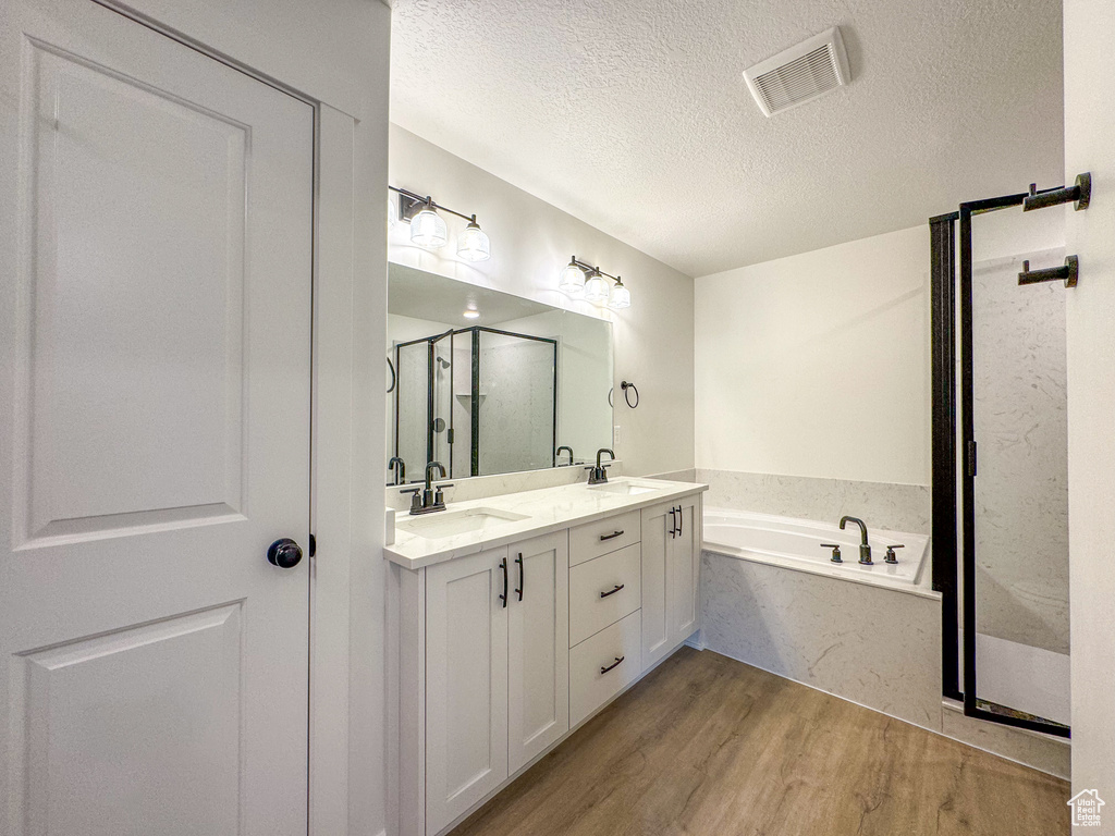 Bathroom featuring independent shower and bath, hardwood / wood-style flooring, double vanity, and a textured ceiling