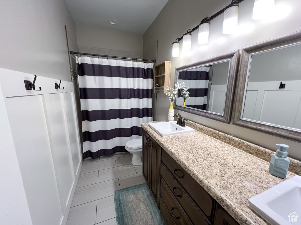 Bathroom with oversized vanity, toilet, dual sinks, and tile flooring