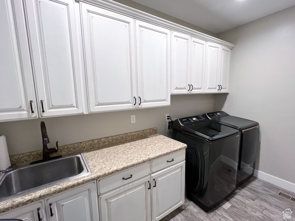 Clothes washing area featuring washing machine and dryer, light hardwood / wood-style floors, cabinets, and sink